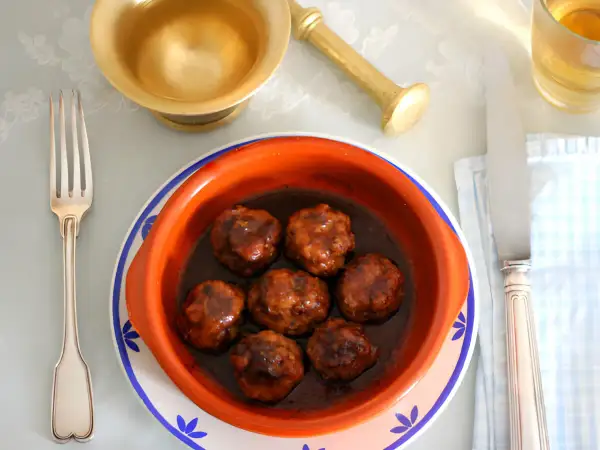Un cuenco de barro con deliciosas albóndigas en salsa, listo para ser disfrutado con tenedor y cuchillo.
