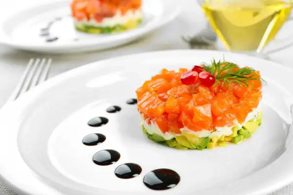 Delicioso tartar de salmón con aguacate, coronado con granada y eneldo. Un plato elegante con un toque de salsa balsámica.