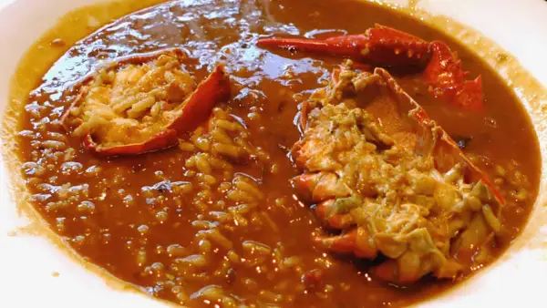 Delicioso arroz caldoso de marisco con trozos de langosta en un plato blanco.