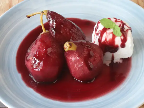 Peras al vino, tiernas y brillantes, bañadas en su jugo rojo, acompañadas de helado y menta.