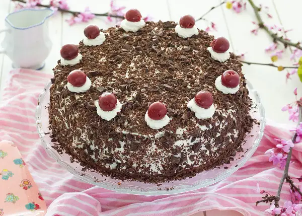 Deliciosa tarta Selva Negra, cubierta de virutas de chocolate y coronada con cerezas y nata. Perfecta para cualquier celebración.