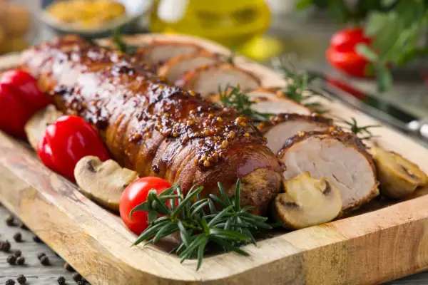 Lomo de cerdo al horno jugoso, glaseado y especiado, servido con champiñones, pimientos rojos y romero en tabla de madera.