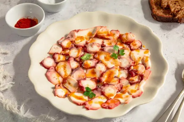 Delicioso carpaccio de pulpo con pimentón y perejil, servido en plato blanco. Acompañado de pan tostado y especias.