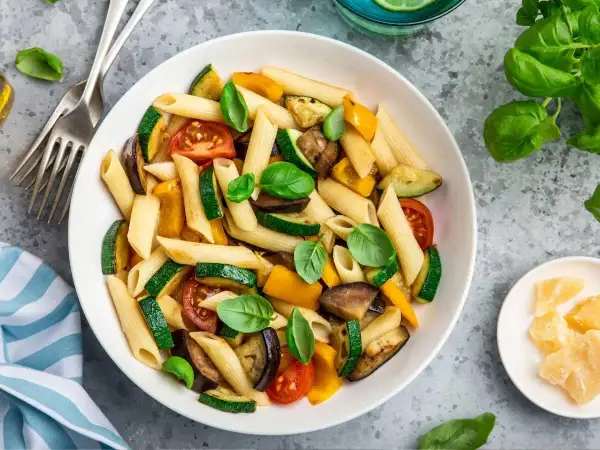 Macarrones con verduras asadas: calabacín, berenjena, pimientos y tomates, decorados con albahaca fresca. ¡Una forma deliciosa de aprender como hacer macarrones!