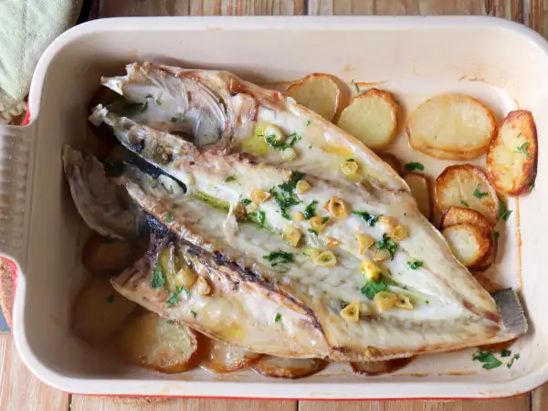 Lubina a la espalda horneada con patatas, ajo y perejil en una bandeja.