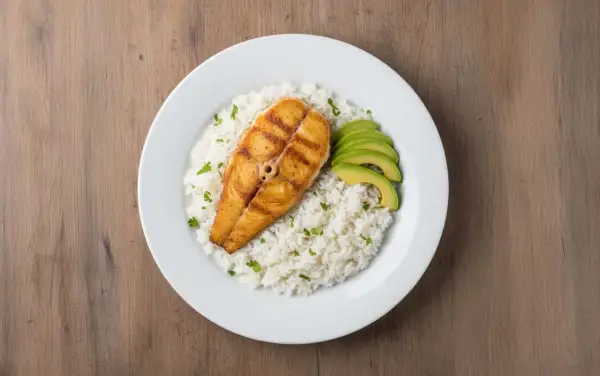 Un delicioso plato de arroz con pescado a la parrilla, acompañado de aguacate en rodajas y perejil picado.