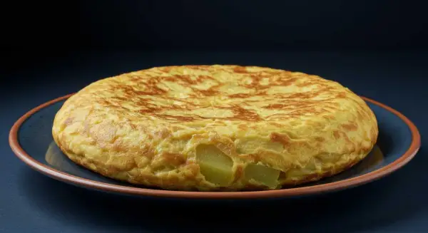 Tortilla de berenjena dorada y esponjosa, con trozos de patata visibles, servida en un plato azul.