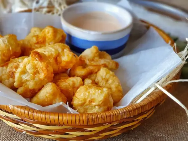 Cesta de mimbre con fritos de pixin dorados y crujientes, acompañados de una salsa rosada. ¡Un bocado delicioso!