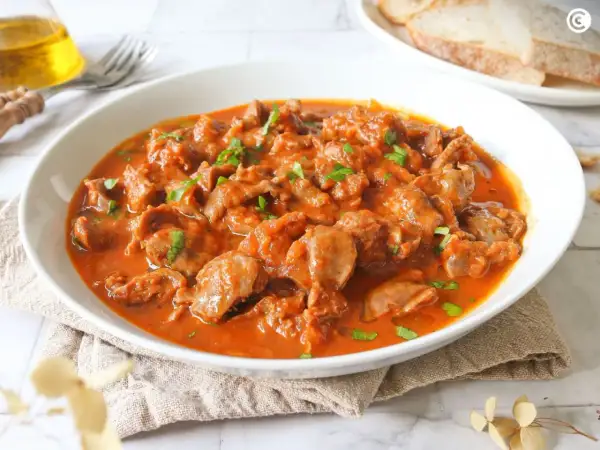Mollejas de pollo en salsa roja, un plato casero y reconfortante, servido en un cuenco blanco con perejil picado.