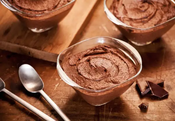 Delicioso mousse de chocolate en copas de cristal, listo para disfrutar. Trozos de chocolate negro al lado.
