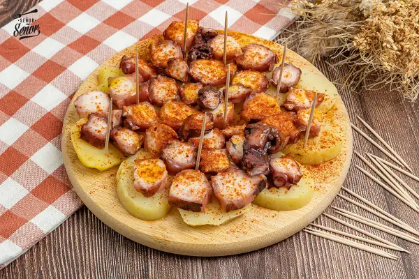 Pulpo a la gallega servido sobre patatas cocidas, espolvoreado con pimentón y servido con palillos.