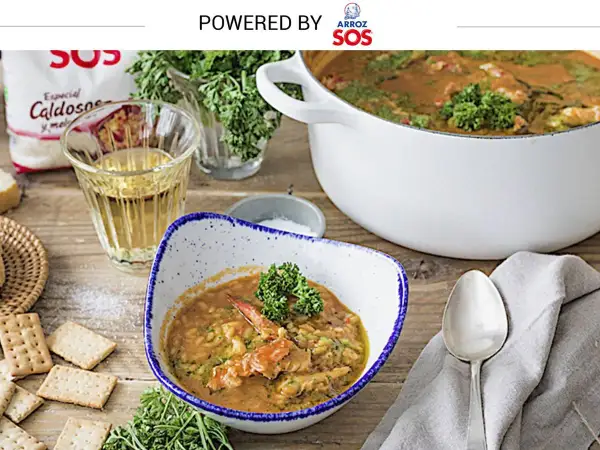 Un delicioso arroz con bogavante, servido en un cuenco con perejil fresco. A su lado, galletas saladas y una copa de vino blanco.