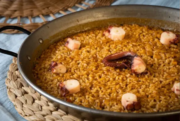 Arroz con pulpo en paellera, con trozos de pulpo bien visibles entre el arroz dorado.