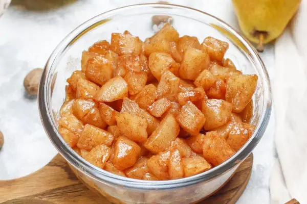 Trozos de manzana asada en freidora de aire, cubiertos de canela, en un bol de cristal.