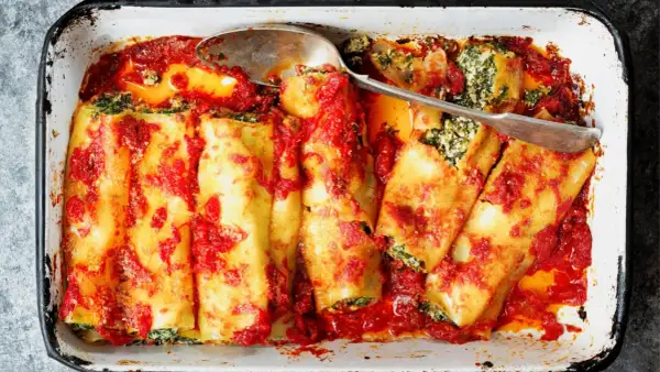 Canelones de atún horneados con salsa de tomate y espinacas, listos para servir en una bandeja.