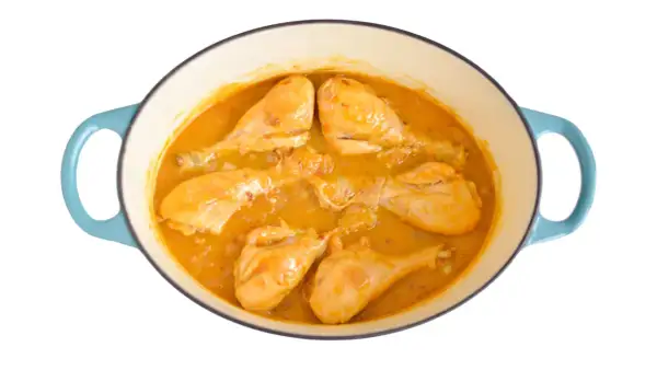 Pollo en salsa dorada, cocinándose en una olla azul. Las piezas de pollo están tiernas y cubiertas de una rica salsa.