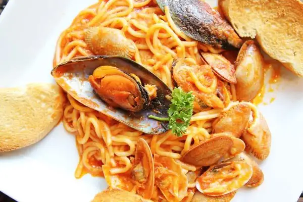 Espaguetis con almejas y mejillones en salsa roja, servidos con pan tostado. Un plato de pasta marinera delicioso.