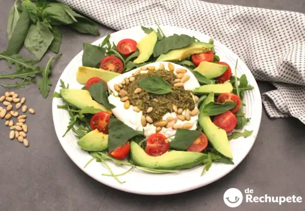 Deliciosa ensalada de burrata y pesto, con aguacate, tomates cherry y piñones.