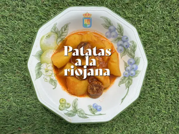 Un plato de patatas a la riojana, con trozos de chorizo y patata en una salsa rojiza, servido en una vajilla decorada con frutas y bayas.