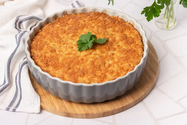 Pastel de bacalao dorado y crujiente, recién horneado en un molde gris, decorado con perejil fresco.