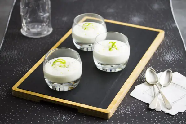 Tres vasitos de cremoso mousse de limón, decorados con ralladura verde, listos para disfrutar.