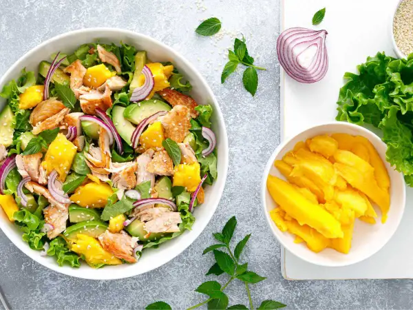 Ensalada de mango con salmón desmenuzado, aguacate, cebolla morada y hojas verdes. ¡Una explosión de sabor!