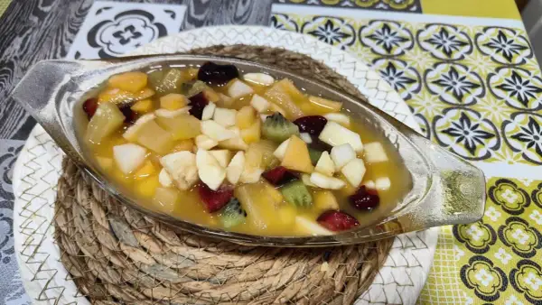 Deliciosa macedonia de frutas en un cuenco de cristal, con trozos de kiwi, plátano, manzana y frutos rojos en almíbar.