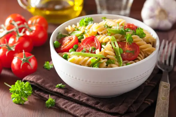 Un delicioso plato de pasta con verduras frescas, tomates cherry, guisantes y perejil.