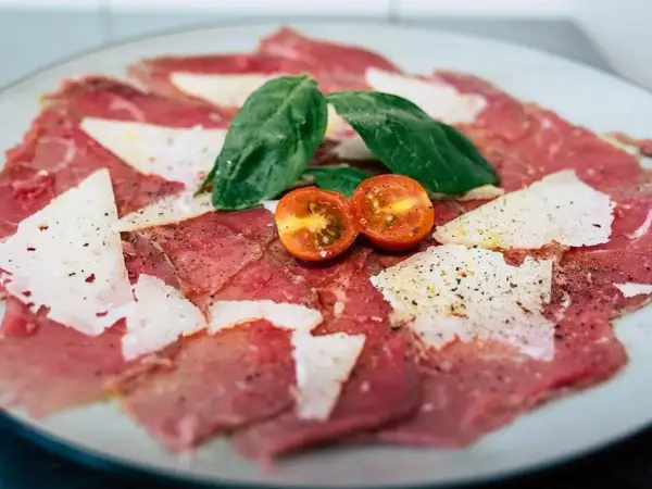Delicado carpaccio de ternera con lascas de parmesano, hojas de albahaca y tomates cherry.
