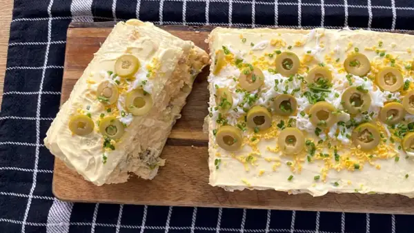 Un delicioso pastel de atún, decorado con aceitunas, huevo rallado y cebollino.