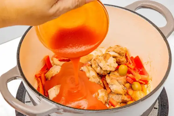 Se vierte salsa de tomate sobre trozos de pollo y pimientos en una olla.