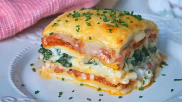 Porción de lasaña de espinacas, con capas de pasta, salsa de tomate, queso derretido y espinacas, espolvoreada con cebollín.