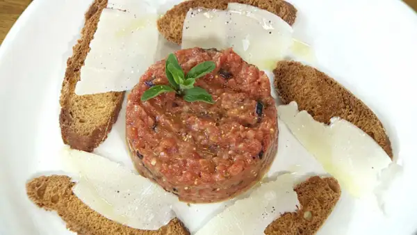 Tartar de tomate fresco, servido con finas láminas de queso y tostadas crujientes. Un bocado ligero y lleno de sabor.