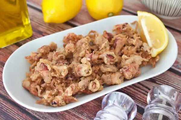 Crujientes puntillas de calamar fritas en un plato blanco, acompañadas de limón y aceite de oliva.