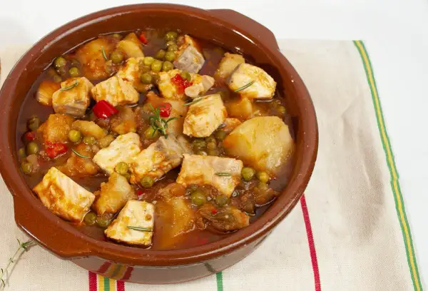Un delicioso marmitako de salmón, con trozos de pescado, patatas, guisantes y pimientos rojos en una cazuela de barro.