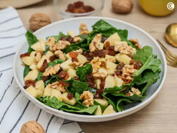 Deliciosa ensalada de espinacas con trozos de manzana, pasas y nueces. Una combinación crujiente y dulce.