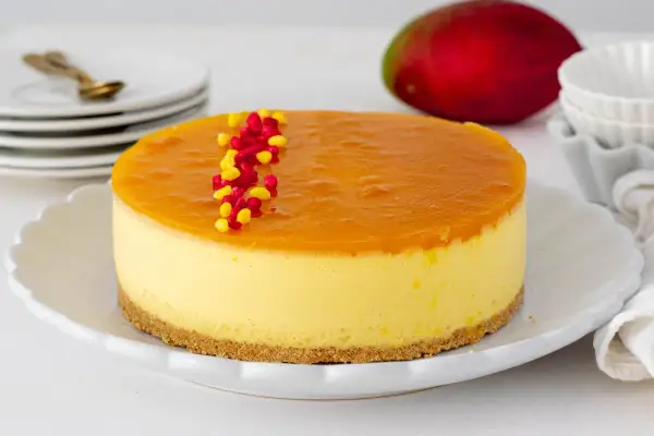 Deliciosa tarta de mango con una capa superior de gelatina brillante y decorada con granos rojos y amarillos.