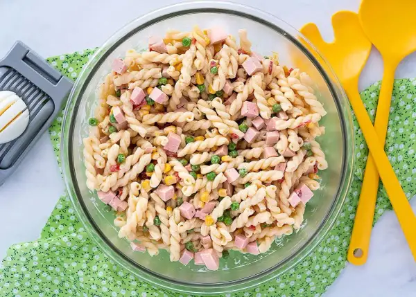 Ensalada de pasta con jamón, guisantes y maíz, lista para servir con su salsa para ensalada de pasta.
