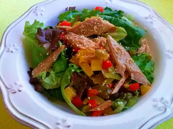 Ensalada de ventresca con pimientos de colores y semillas de sésamo, servida sobre hojas verdes frescas.