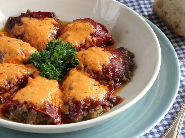 Pimientos rellenos de carne cubiertos con una cremosa salsa, decorados con perejil fresco.