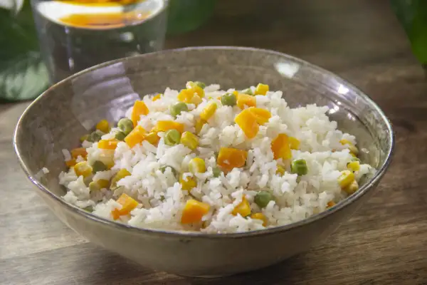 Un plato de arroz blanco con guisantes, maíz y zanahoria en cubitos. Una receta de arroz con verduras sencillo y colorido.