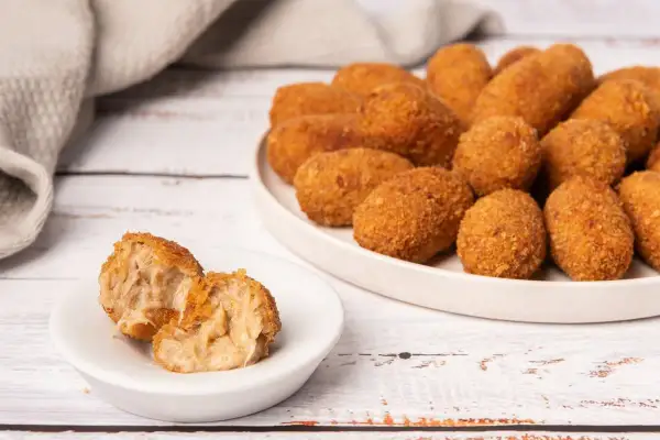 Croquetas de puchero doradas y crujientes, una de ellas partida mostrando su interior cremoso.