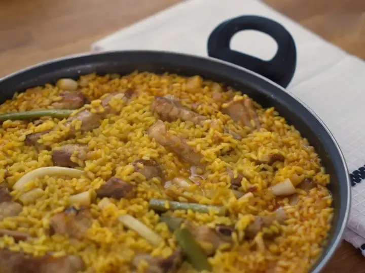 Paella recién hecha, un plato perfecto para tus recetas de arroz. Con trozos de carne, judías verdes y un arroz amarillo vibrante.