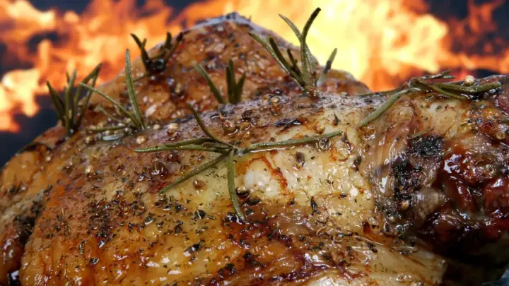Pierna de cordero al horno, dorada y jugosa, con romero y especias, sobre un fondo de llamas. ¡Un festín irresistible!